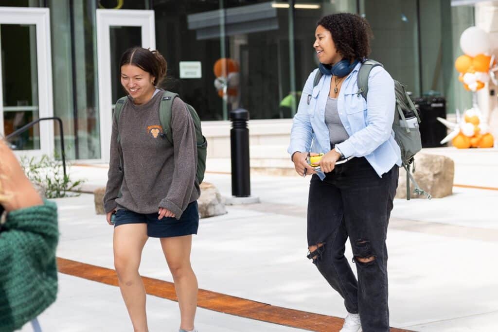 Two students walking a laughing together outside the Agriculture and Natural Resources Building, a large glass building on the the UTIA campus.