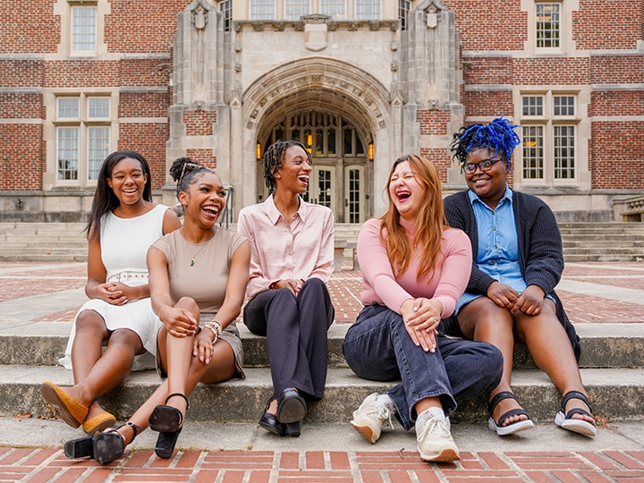 Group of students in the Minorities in Agriculture, Natural Resources and Related Sciences student organization sitting on steps and laughing with a large brick building behind them.