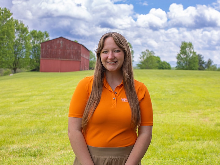Headshot of Abigail Berny wearing a Herbert polo in a field with a red barn in the background.