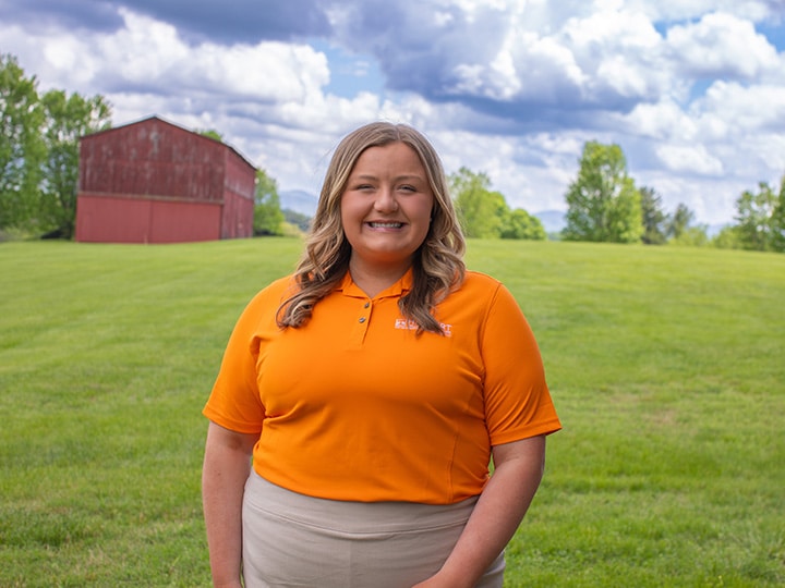Headshot of Alice Grace Beavers wearing a Herbert polo in a field with a red barn in the background.