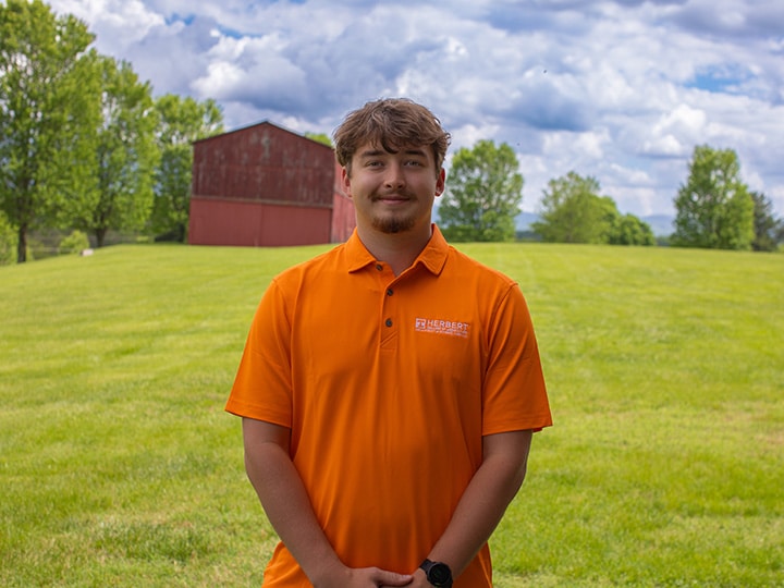 Headshot of Blake Stoner wearing a Herbert polo in a field with a red barn in the background.