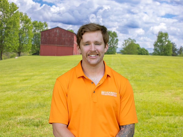 Headshot of Brendan Hogan wearing a Herbert polo in a field with a red barn in the background.
