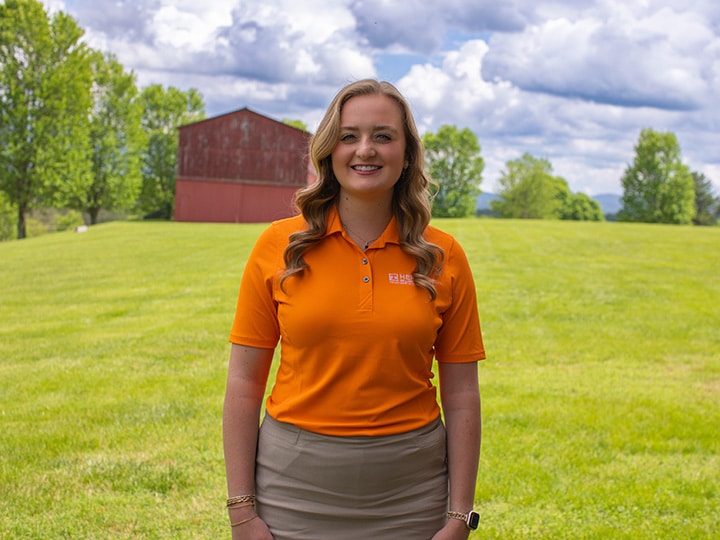 Headshot of Callie Hudson wearing a Herbert polo in a field with a red barn in the background.