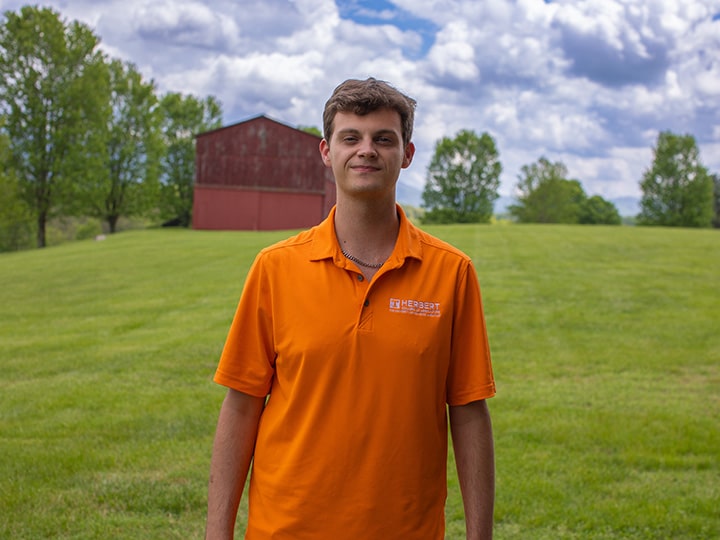 Headshot of Campbell Emerson wearing a Herbert polo in a field with a red barn in the background.