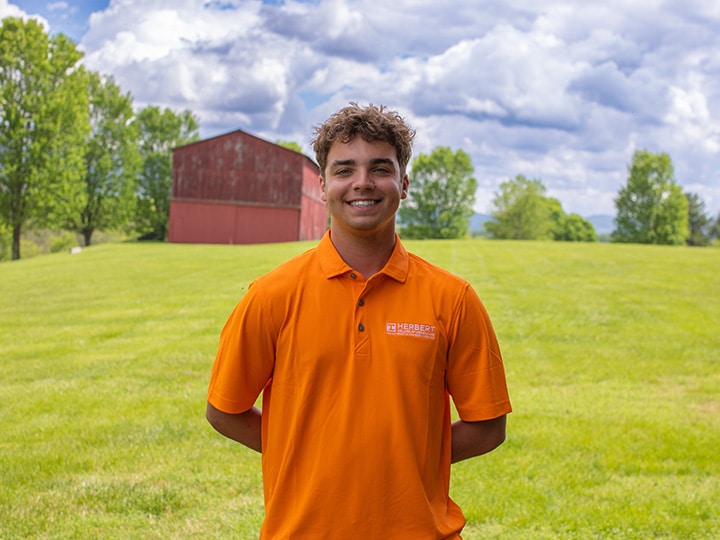 Headshot of Cooper Zale wearing a Herbert polo in a field with a red barn in the background.