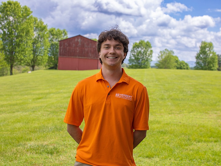 Headshot of Drew Hogan wearing a Herbert polo in a field with a red barn in the background.