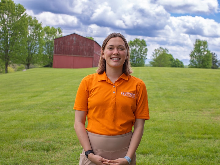 Headshot of Finley Oldham wearing a Herbert polo in a field with a red barn in the background.