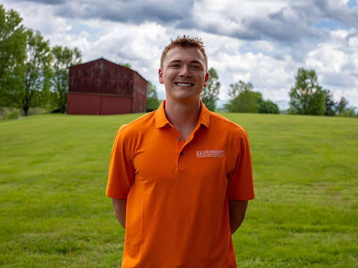 Headshot of Garrett Reeves wearing a Herbert polo in a field with a red barn in the background.
