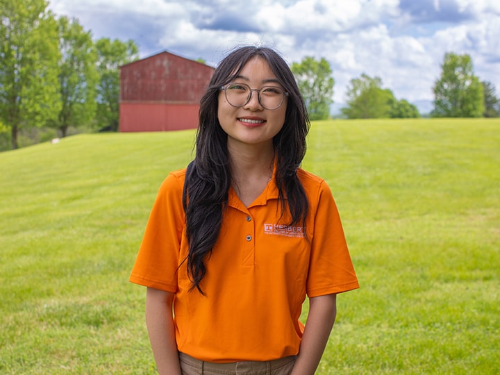 Headshot of Kaitlyn Choi wearing a Herbert polo in a field with a red barn in the background.