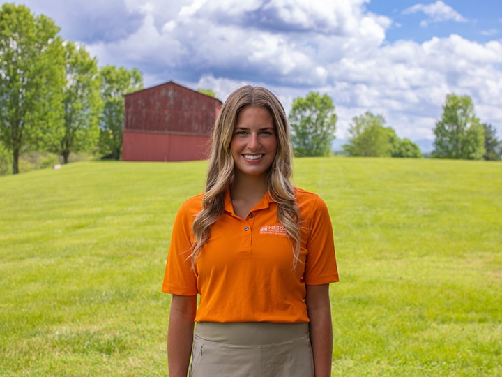 Headshot of Kate Gourley wearing a Herbert polo in a field with a red barn in the background.