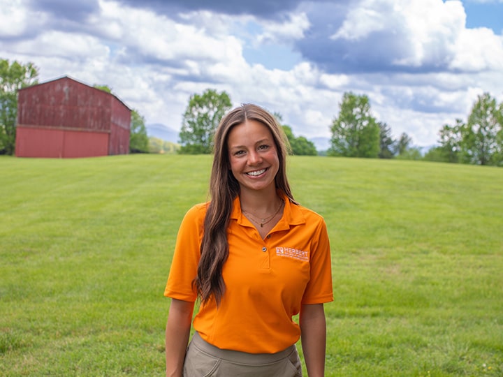 Headshot of Kaylea Fields wearing a Herbert polo in a field with a red barn in the background.
