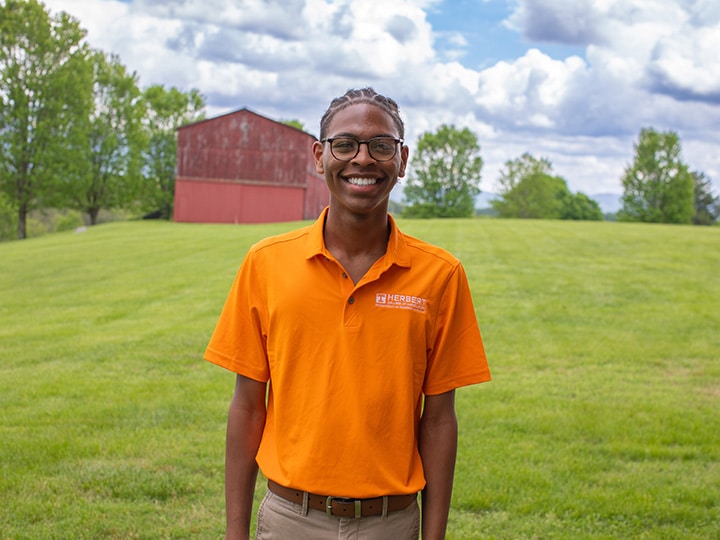 Headshot of Kendall Beard wearing a Herbert polo in a field with a red barn in the background.