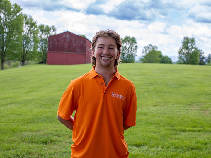 Headshot of Lewis Brooke wearing a Herbert polo in a field with a red barn in the background.