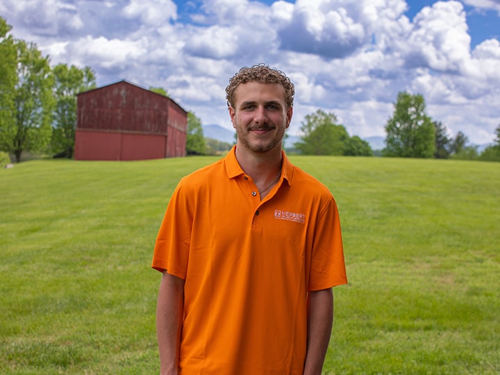 Headshot of Luke Davis wearing a Herbert polo in a field with a red barn in the background.