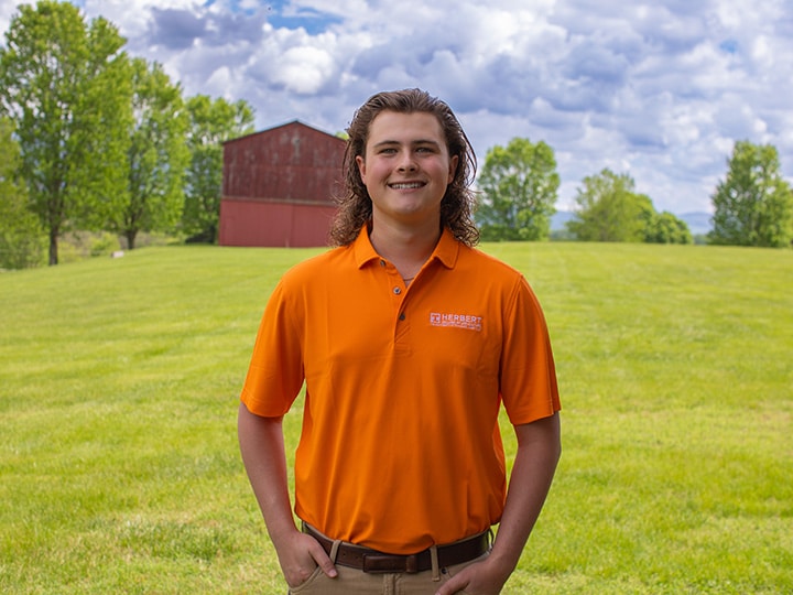 Headshot of Rhyder Short wearing a Herbert polo in a field with a red barn in the background.