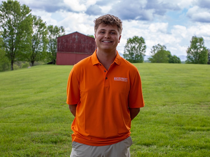 Headshot of Sawyer Stephens wearing a Herbert polo in a field with a red barn in the background.