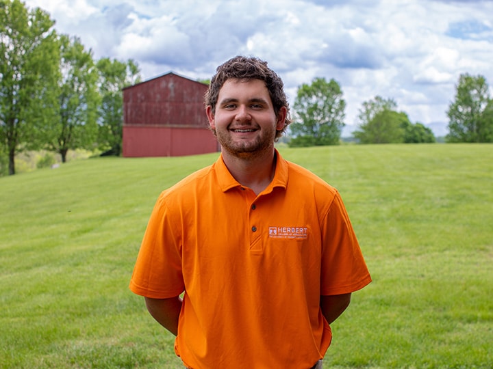 Headshot of Tate Kerns wearing a Herbert polo in a field with a red barn in the background.