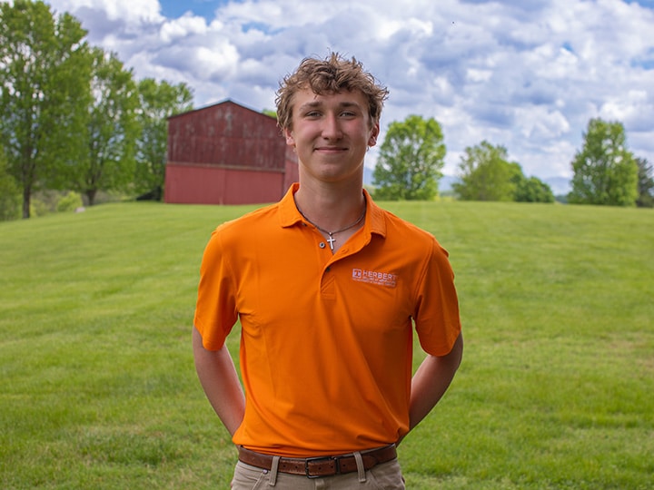 Headshot of Will Aukema wearing a Herbert polo in a field with a red barn in the background.