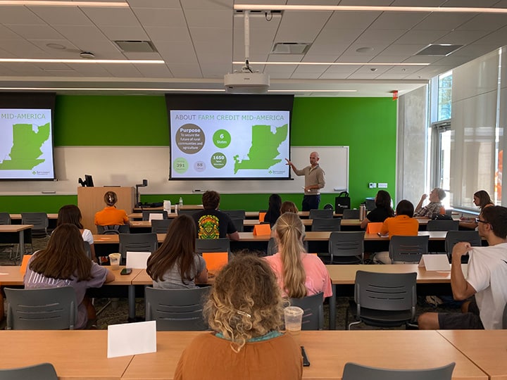 Students in a classroom looking at a screen that reads "About Farm Credit Mid-America" with a green wall behind it.