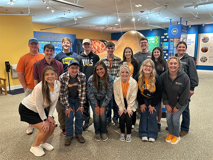 A group of students taking a group photo at the Bush's Baked Beans headquarters with a giant bean statue behind them.