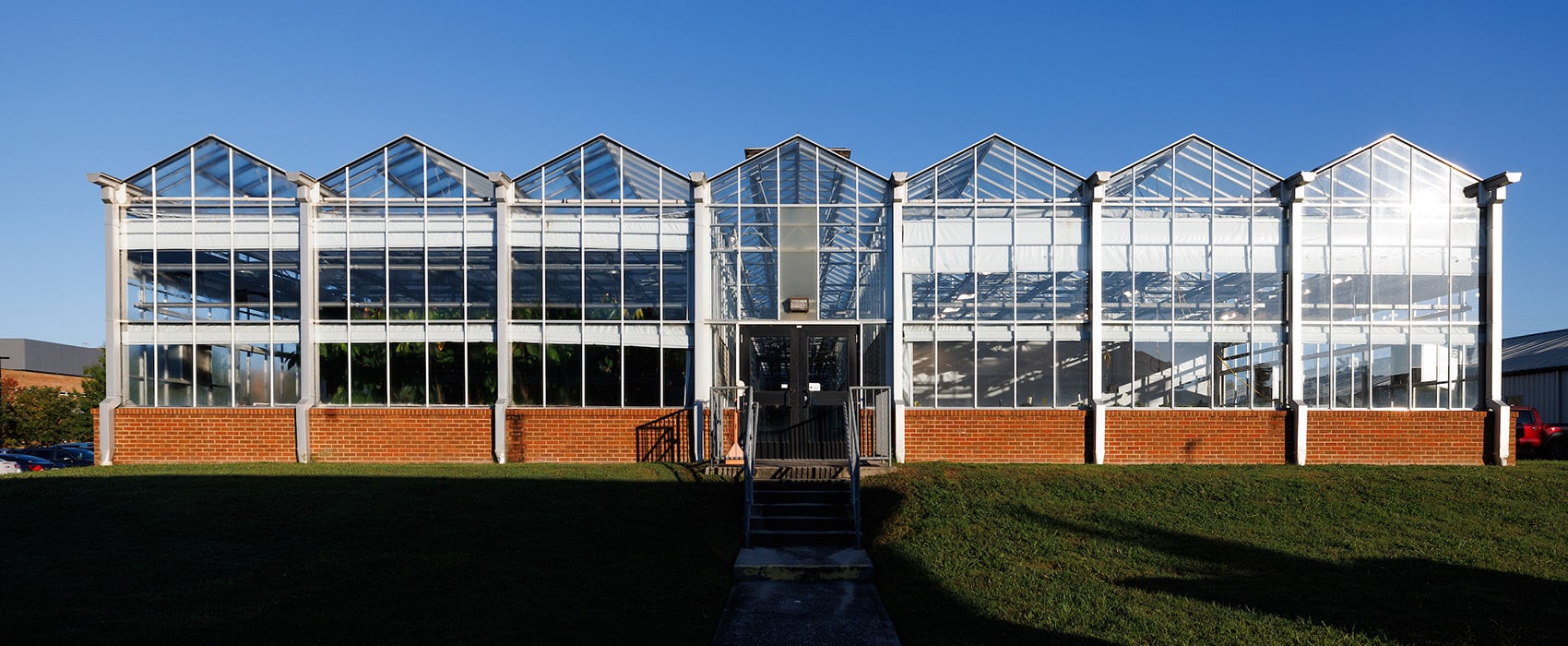 A greenhouse with red brick at the bottom on a sunny day with a clear blue sky.
