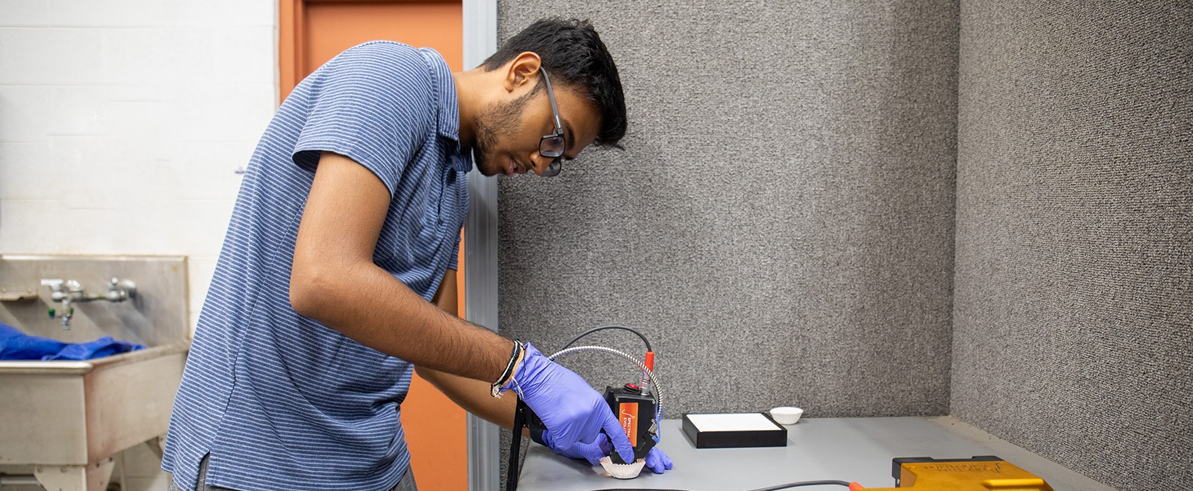 Student wearing a blue striped shirt using equipment for research in a lab setting.
