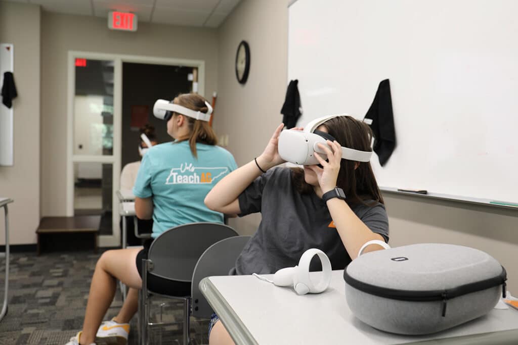 Students in a classroom wearing virtual reality goggles with one student wearing a shirt that says "Vols Teach Ag" on the back.