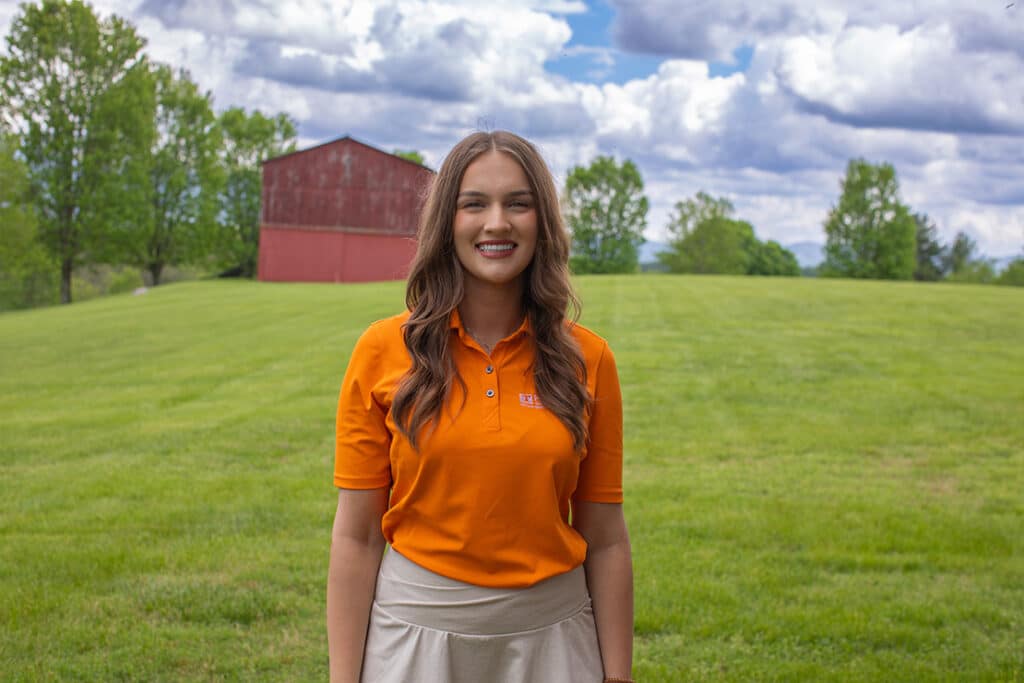 Headshot of Abby Hamm wearing an orange polo with a red barn in the background.