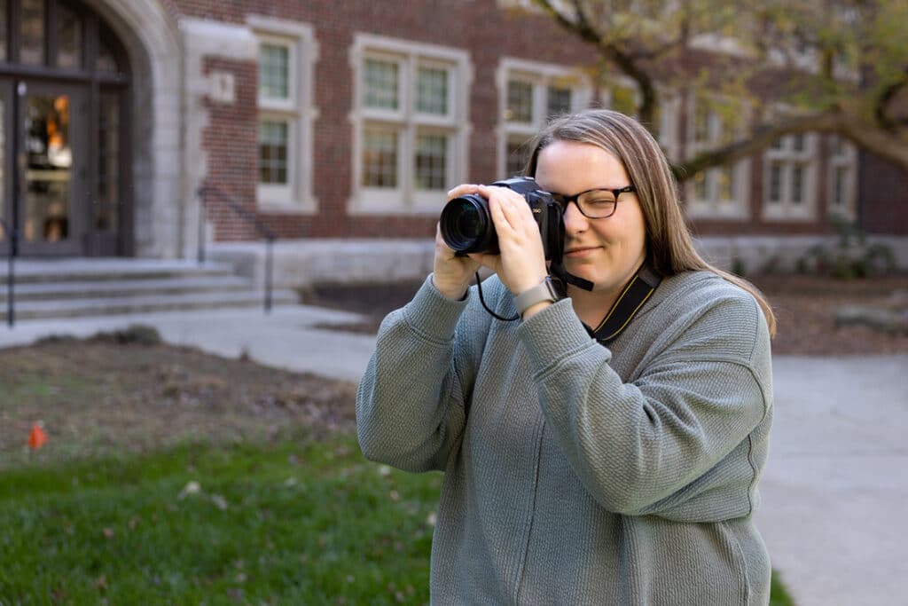A student using a professional camera outside a brick building.