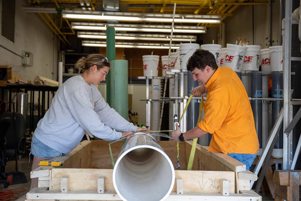 Two biosystems engineering students working on their senior design project, which includes a large white tubular structure.