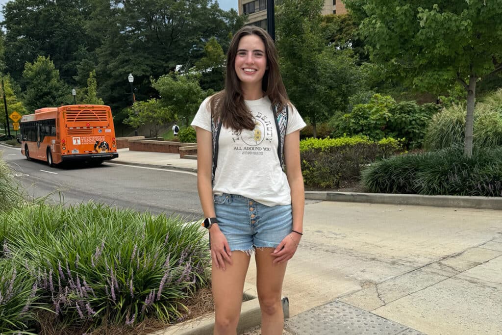 Biosystems engineering student Emily Ellis standing outside at UT's campus with a T-bus in the background.