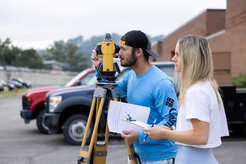 Two construction science and management students participating in a surveying class outside.