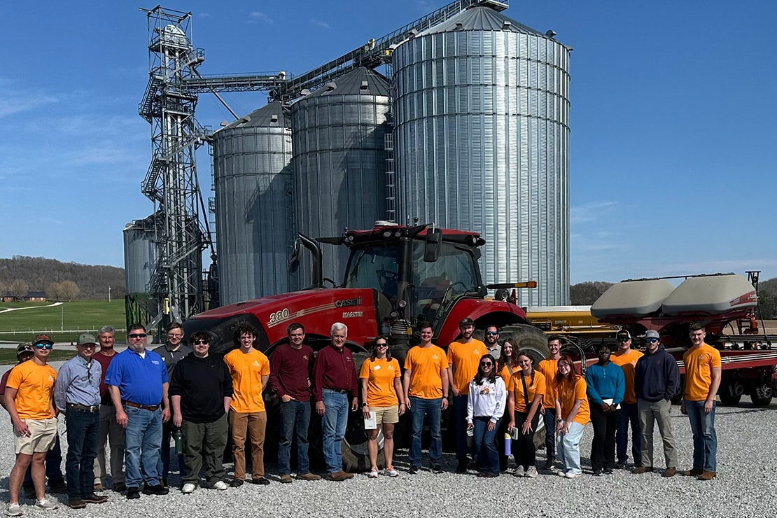 Group of people with some wearing orange shirts standing in front of grain silos.
