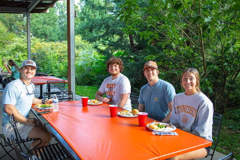 Four graduate students sitting at an outdoor table eating picnic food.