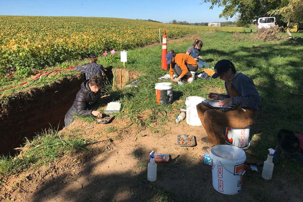 Students outside on a sunny day testing soil samples with white and orange Tennessee Soil Vols buckets.
