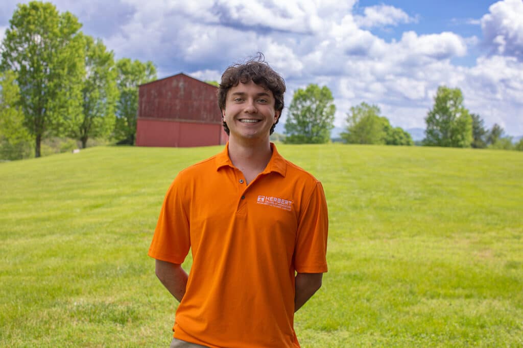 Headshot of Drew Hogan wearing a Herbert polo in a field with a red barn in the background.