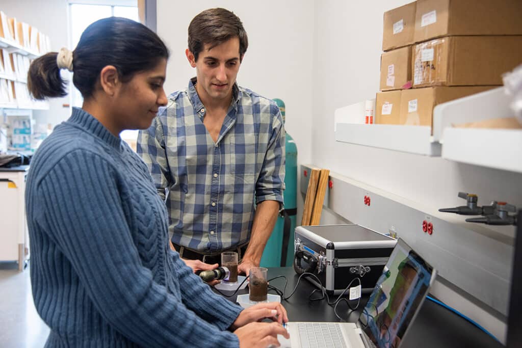 Two graduate students looking at a computer as they test soil in a lab setting.