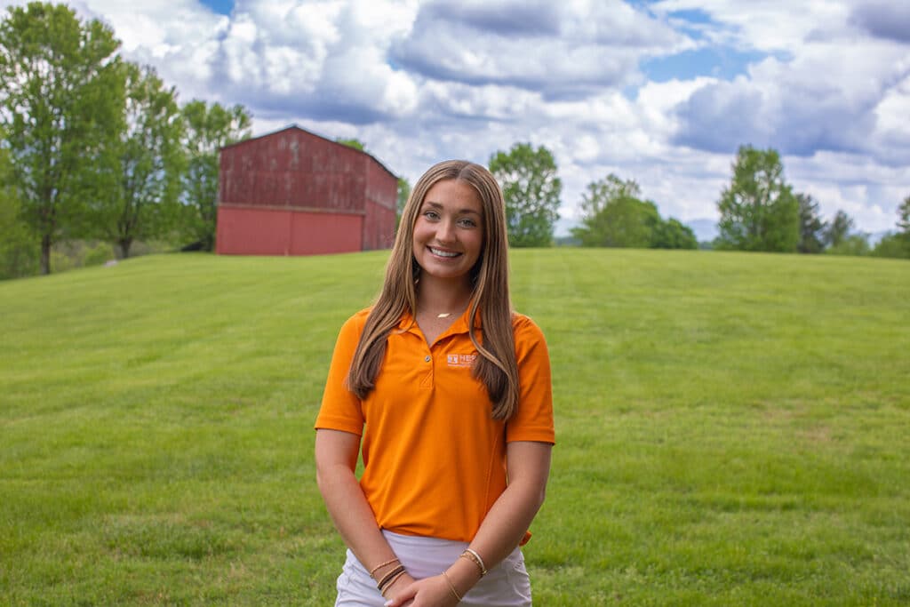 Headshot of Taylor Bundy wearing a Herbert polo in a field with a red barn in the background.