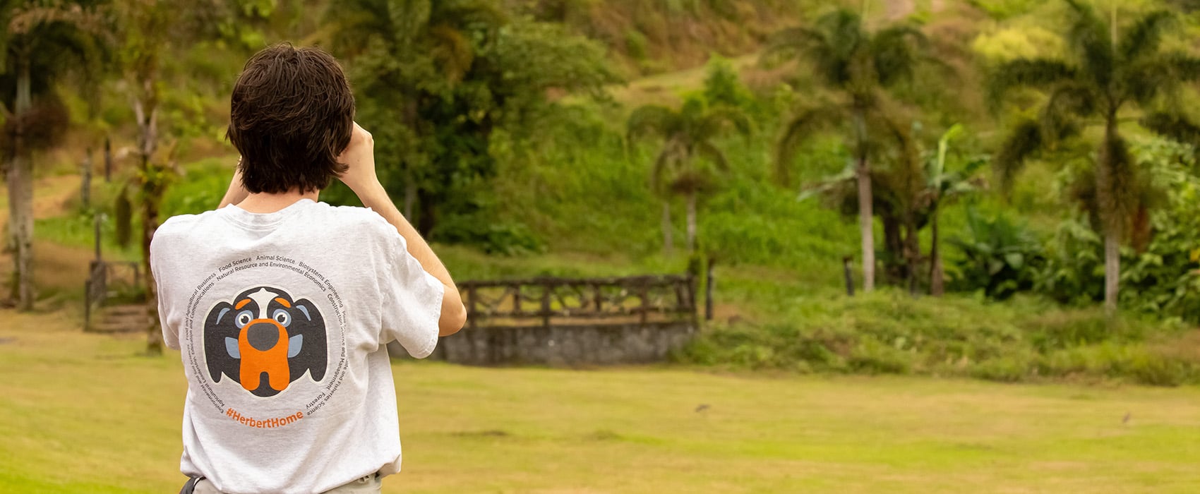 A first-year Herbert College of Agriculture student looking at a Costa Rican landscape wearing a white shirt with a Smokey graphic on the back.
