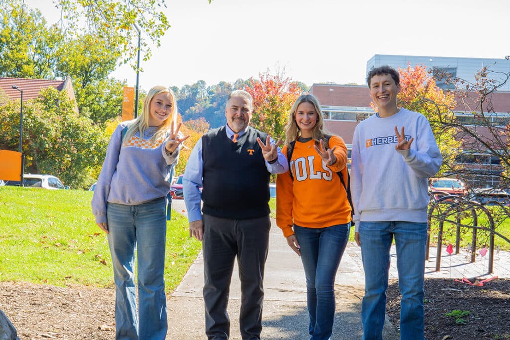 Dean David White holding up the "Vols" sign with three students outside Morgan Hall.