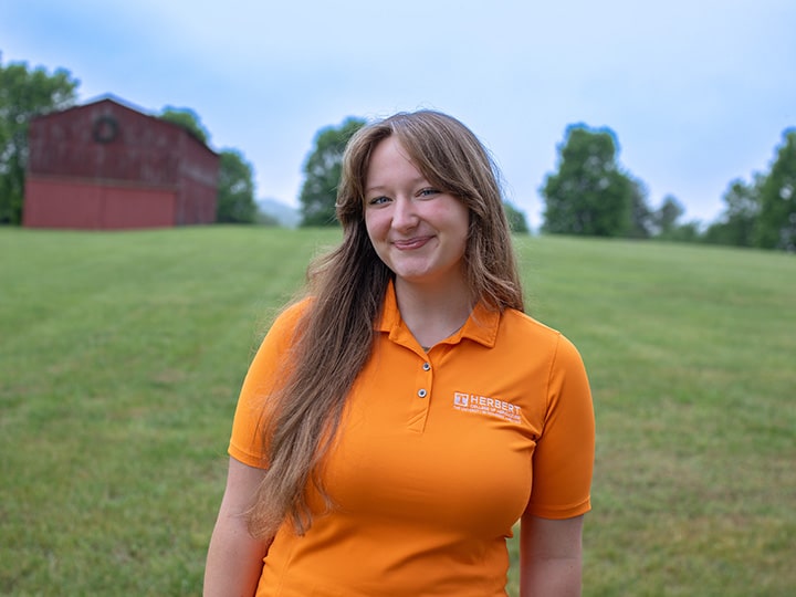 Headshot of Abigail Berny wearing a Herbert polo in a field with a red barn in the background.