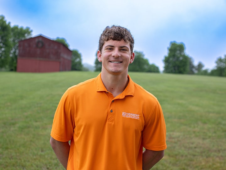 Headshot of Alex Katzakian wearing a Herbert polo in a field with a red barn in the background.