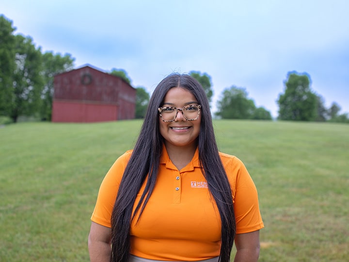 Headshot of Ariana Mota wearing a Herbert polo in a field with a red barn in the background.