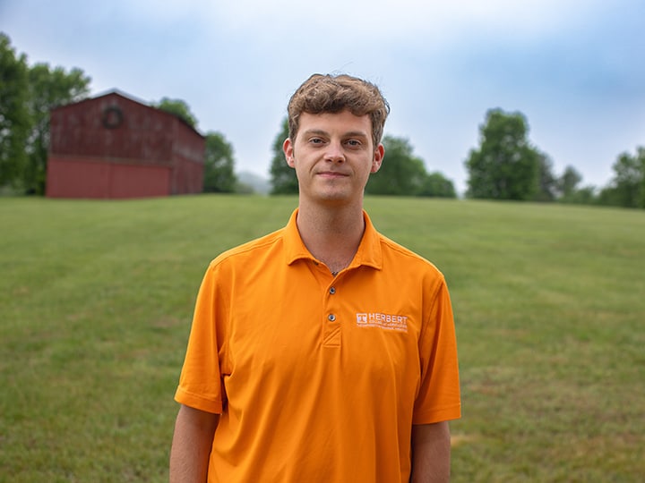Headshot of Campbell Emerson wearing a Herbert polo in a field with a red barn in the background.