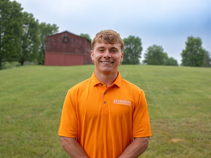 Headshot of Connor Reeves wearing a Herbert polo in a field with a red barn in the background.