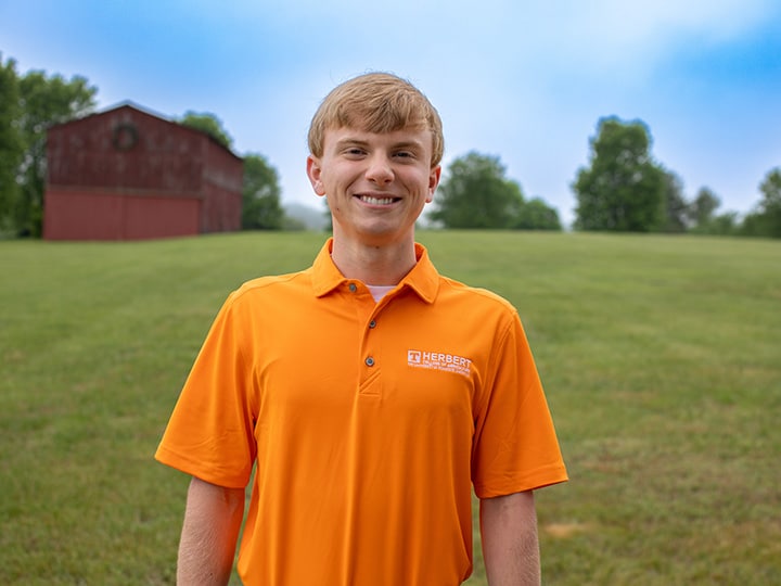 Headshot of Gabe Harville wearing a Herbert polo in a field with a red barn in the background.