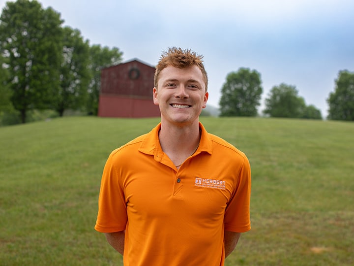 Headshot of Garrett Reeves wearing a Herbert polo in a field with a red barn in the background.