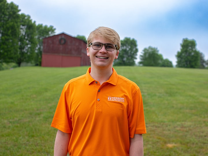 Headshot of Gavin Higgins wearing a Herbert polo in a field with a red barn in the background.