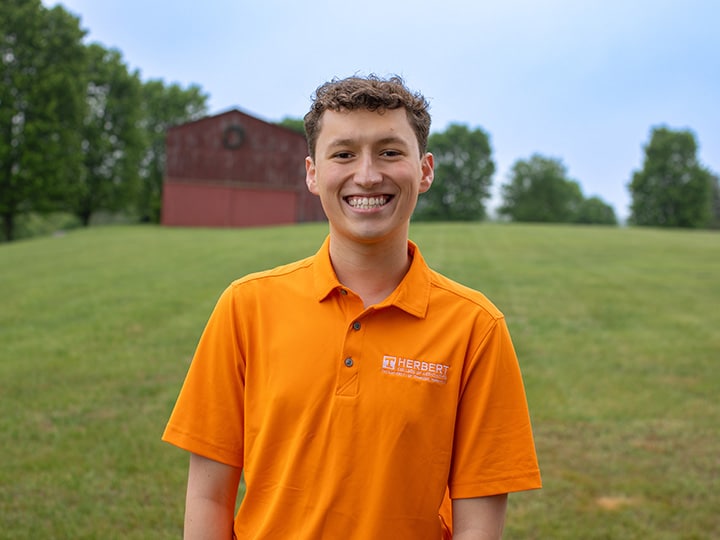 Headshot of George William Wilson wearing a Herbert polo in a field with a red barn in the background.