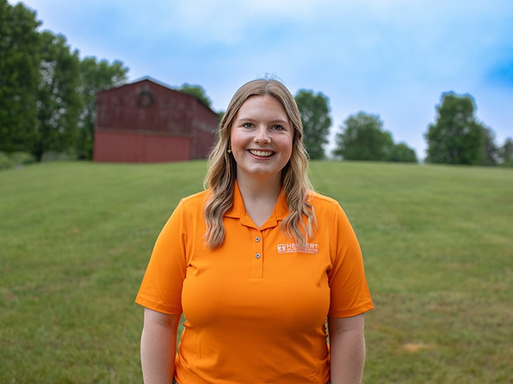 Headshot of Kaylee Garrell wearing a Herbert polo in a field with a red barn in the background.